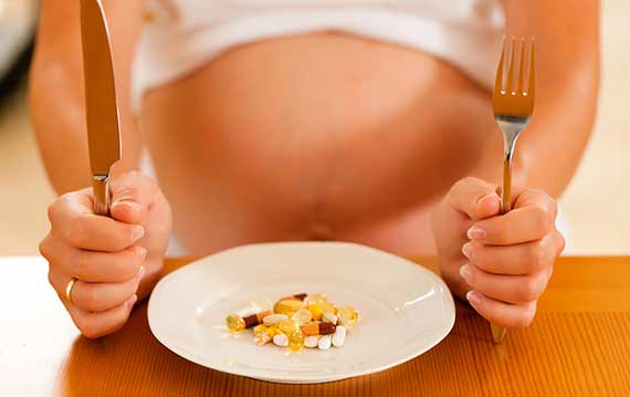 Gravid kvinde med vitaminer på tallerken.